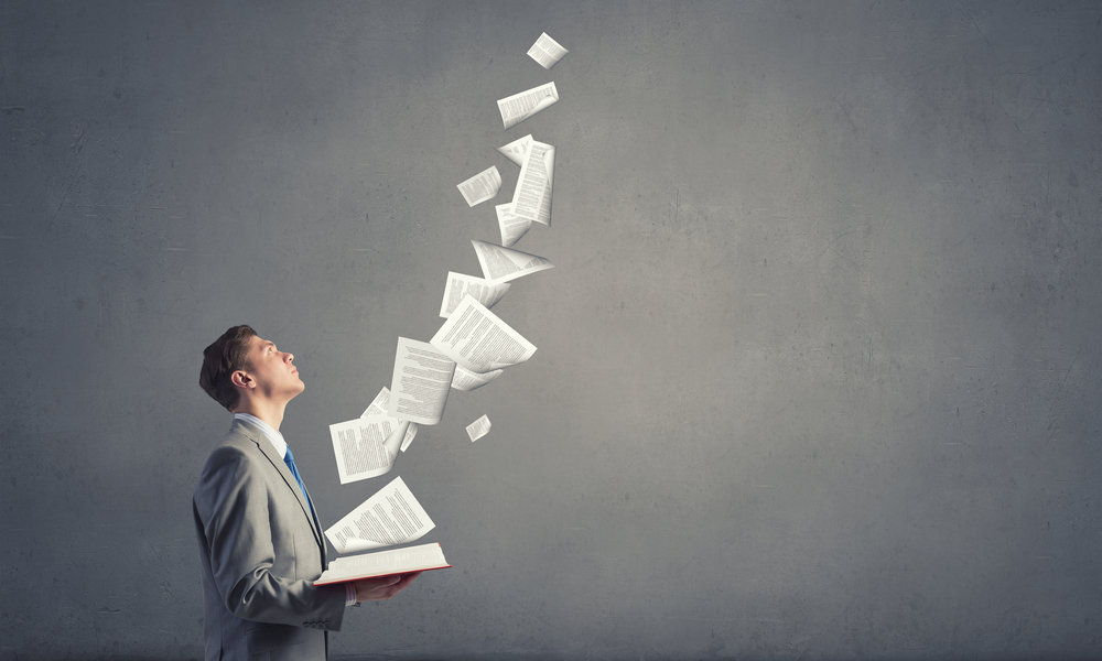 Young businessman with opened book in hands and pages flying in air